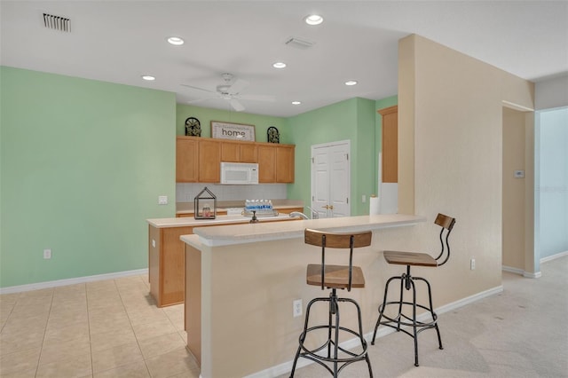 kitchen featuring ceiling fan, tasteful backsplash, light colored carpet, kitchen peninsula, and a kitchen breakfast bar