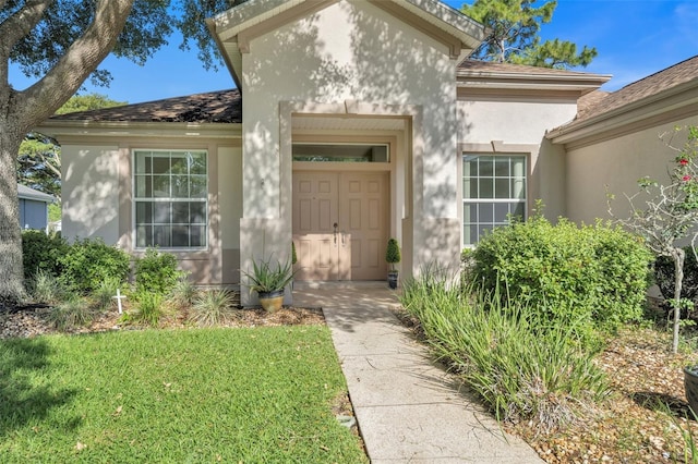 property entrance featuring a garage, stucco siding, a yard, and roof with shingles