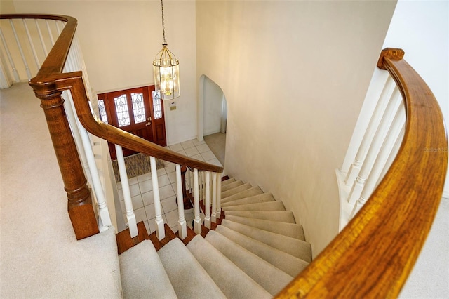 stairway featuring carpet floors, a notable chandelier, and a high ceiling