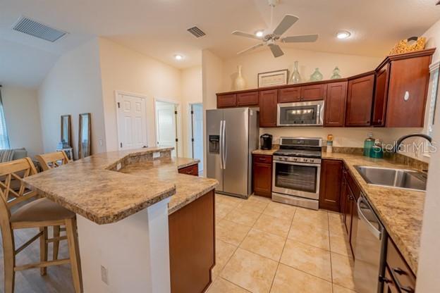 kitchen featuring lofted ceiling, sink, light tile patterned floors, a breakfast bar area, and appliances with stainless steel finishes