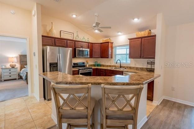 kitchen with sink, vaulted ceiling, appliances with stainless steel finishes, a kitchen breakfast bar, and dark stone counters