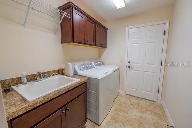 laundry area featuring sink, light tile patterned floors, washer and clothes dryer, and cabinets