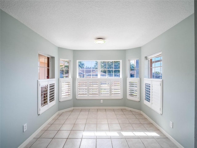 spare room featuring light tile patterned floors, a textured ceiling, and baseboards