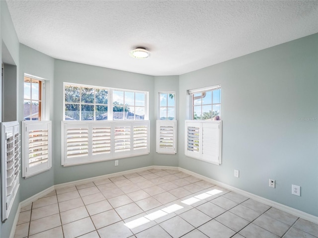 spare room with a textured ceiling, light tile patterned flooring, and baseboards