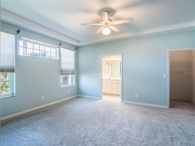 unfurnished bedroom with light carpet, ensuite bath, a walk in closet, and baseboards