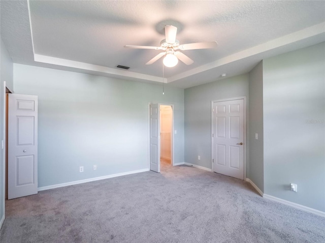 carpeted empty room with baseboards, visible vents, ceiling fan, a tray ceiling, and a textured ceiling