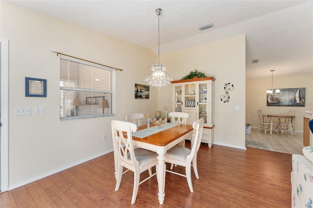 dining room with a textured ceiling, a chandelier, and hardwood / wood-style flooring