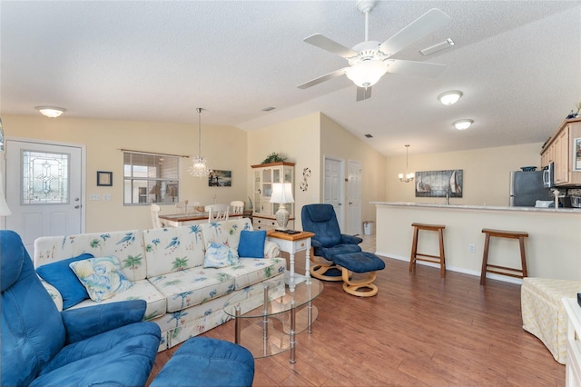 living room with wood-type flooring, vaulted ceiling, ceiling fan with notable chandelier, and a textured ceiling