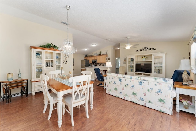 dining room with lofted ceiling, ceiling fan with notable chandelier, a textured ceiling, and hardwood / wood-style floors