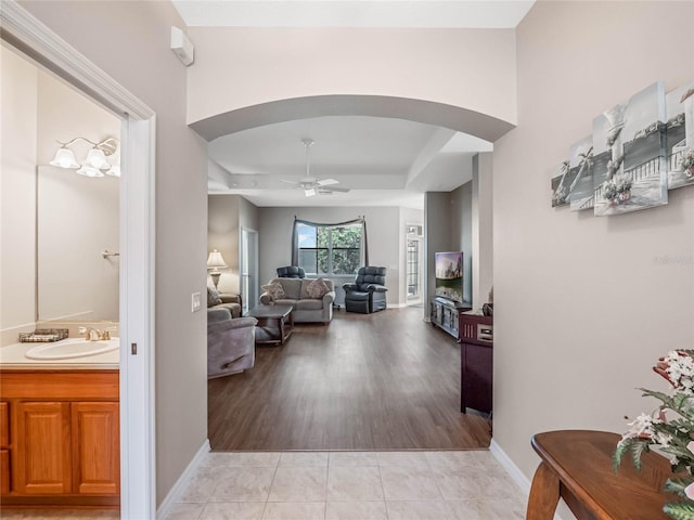 hall featuring light wood-type flooring, a raised ceiling, and sink