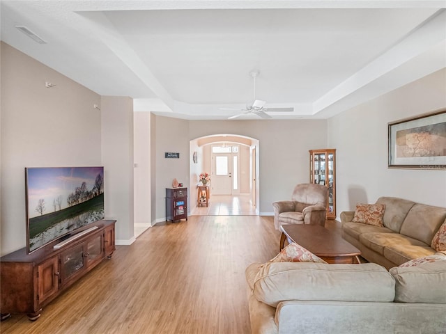 living room featuring ceiling fan, a tray ceiling, and light hardwood / wood-style flooring