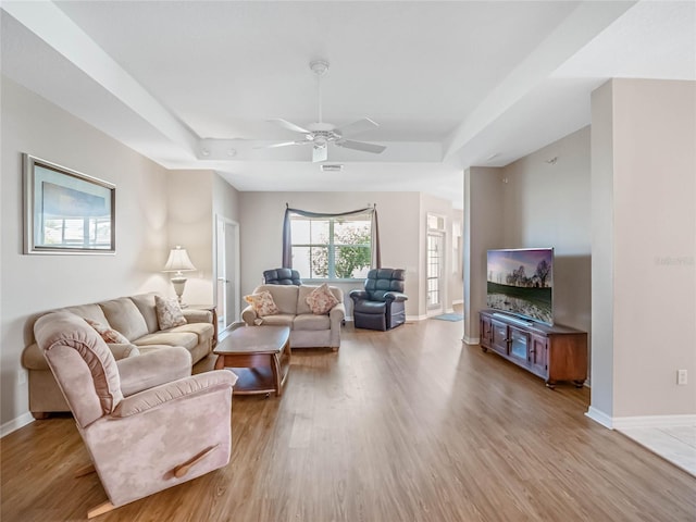 living room featuring a tray ceiling, ceiling fan, and light hardwood / wood-style flooring