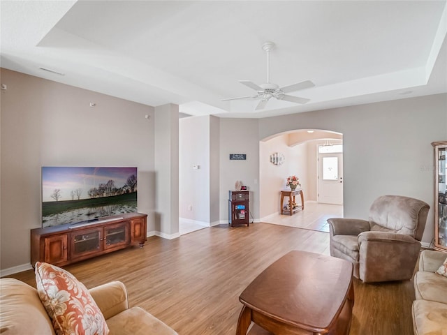 living room with light hardwood / wood-style floors, a raised ceiling, and ceiling fan