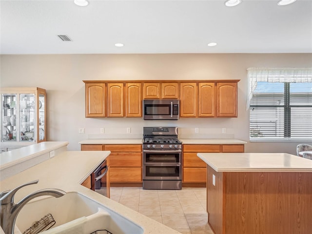 kitchen featuring light tile patterned flooring, a kitchen island, sink, and appliances with stainless steel finishes