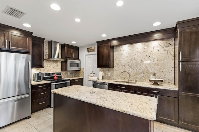 kitchen with light stone counters, a kitchen island, appliances with stainless steel finishes, wall chimney exhaust hood, and sink