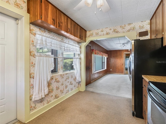 kitchen with light colored carpet, stove, ceiling fan, and wood walls