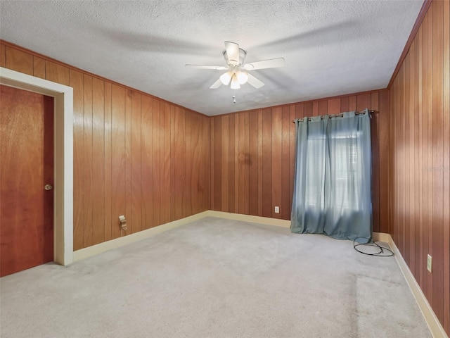 carpeted spare room with ceiling fan, wooden walls, and a textured ceiling