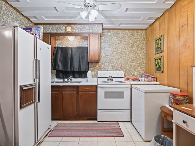 kitchen featuring wood walls, white appliances, light tile floors, sink, and ceiling fan