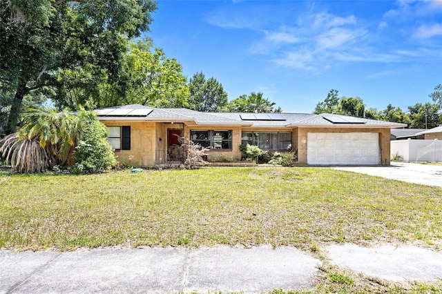 ranch-style home featuring a garage, solar panels, and a front yard