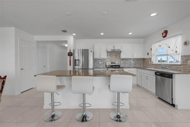 kitchen featuring white cabinets, sink, a kitchen island, stone counters, and appliances with stainless steel finishes