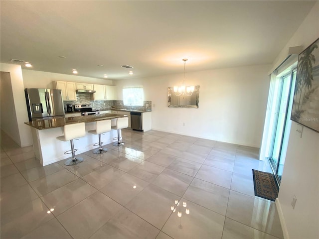 kitchen featuring hanging light fixtures, tasteful backsplash, white cabinetry, appliances with stainless steel finishes, and a kitchen bar