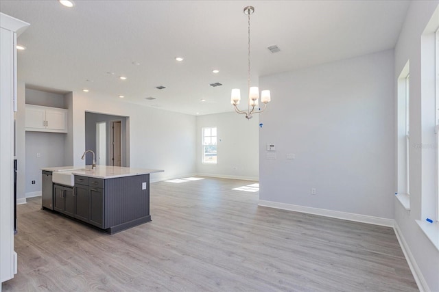 kitchen featuring an island with sink, sink, white cabinets, stainless steel dishwasher, and light wood-type flooring