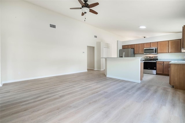 kitchen with appliances with stainless steel finishes, a center island, ceiling fan, a towering ceiling, and light tile flooring