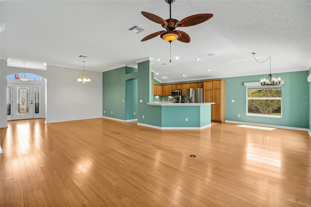 unfurnished living room with ceiling fan with notable chandelier, crown molding, a textured ceiling, and light wood-type flooring