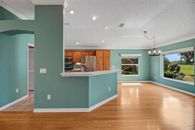 kitchen with appliances with stainless steel finishes, a textured ceiling, light wood-type flooring, decorative light fixtures, and an inviting chandelier