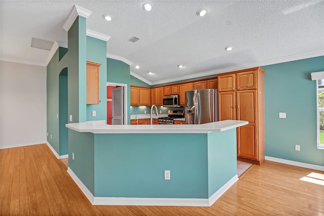 kitchen featuring appliances with stainless steel finishes, light hardwood / wood-style floors, lofted ceiling, ornamental molding, and kitchen peninsula