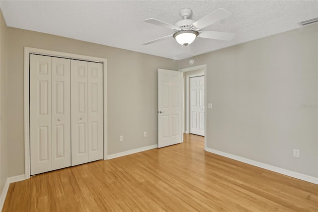 unfurnished bedroom featuring a closet, light hardwood / wood-style flooring, ceiling fan, and a textured ceiling