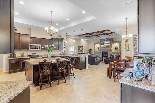 kitchen featuring a center island, light stone countertops, ceiling fan with notable chandelier, stainless steel appliances, and a stone fireplace