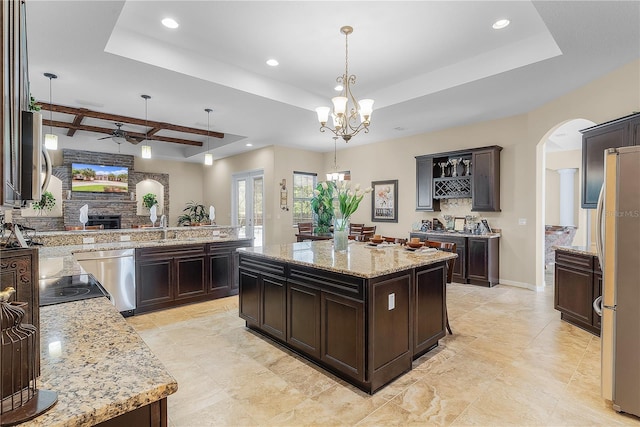 kitchen featuring hanging light fixtures, ceiling fan with notable chandelier, a stone fireplace, and a tray ceiling