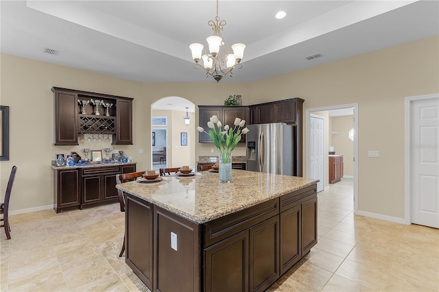 kitchen featuring a kitchen island, light tile flooring, dark brown cabinets, stainless steel fridge with ice dispenser, and light stone countertops