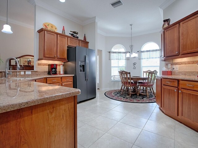 kitchen featuring pendant lighting, visible vents, brown cabinetry, a sink, and black fridge