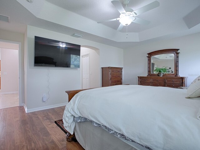 bedroom with arched walkways, a raised ceiling, visible vents, dark wood-type flooring, and baseboards