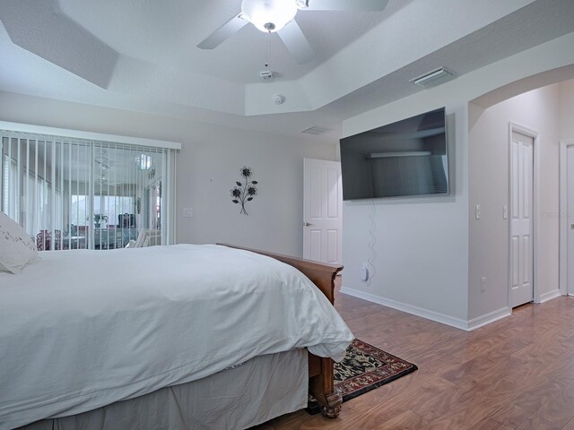 bedroom featuring arched walkways, wood finished floors, visible vents, access to exterior, and a tray ceiling