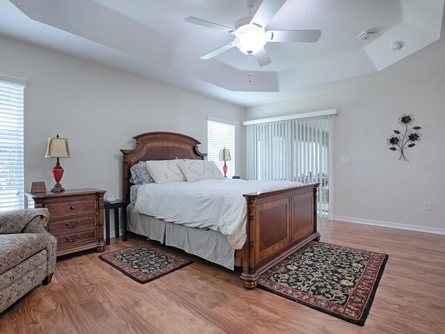 bedroom with a ceiling fan, multiple windows, baseboards, and wood finished floors