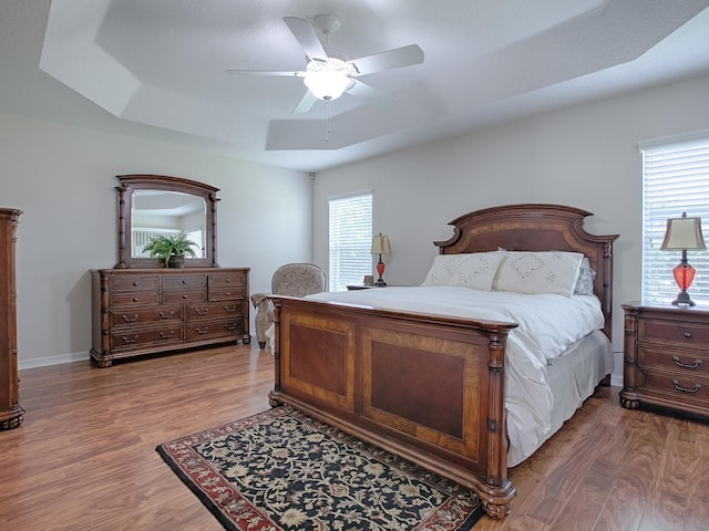 bedroom featuring a ceiling fan, a raised ceiling, baseboards, and wood finished floors