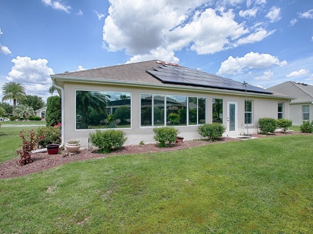 back of property featuring roof mounted solar panels, a lawn, and stucco siding