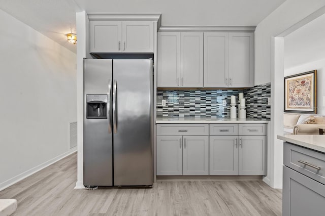 kitchen featuring decorative backsplash, stainless steel fridge, gray cabinets, and light hardwood / wood-style flooring