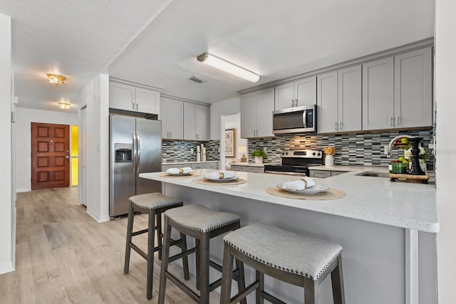 kitchen with gray cabinetry, sink, stainless steel appliances, tasteful backsplash, and light hardwood / wood-style flooring