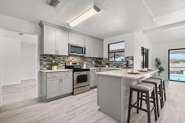 kitchen with gray cabinets, light hardwood / wood-style floors, lofted ceiling, and appliances with stainless steel finishes