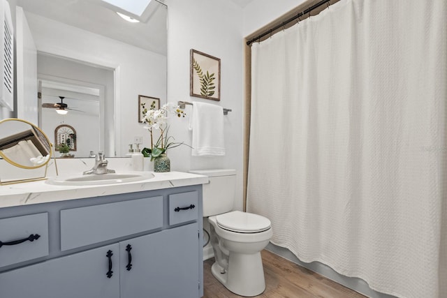 bathroom with a skylight, vanity, ceiling fan, hardwood / wood-style floors, and toilet