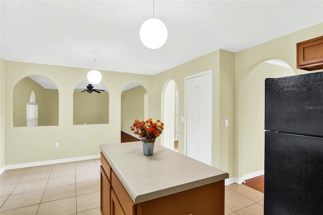 kitchen with ceiling fan, a kitchen island, light tile patterned flooring, black refrigerator, and decorative light fixtures