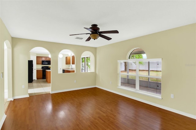 empty room with a wealth of natural light, sink, light hardwood / wood-style floors, and ceiling fan