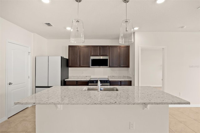 kitchen featuring light stone counters, sink, decorative light fixtures, a center island with sink, and a kitchen bar