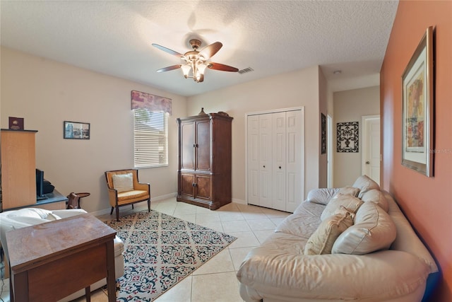 living room featuring ceiling fan, a textured ceiling, and light tile patterned floors