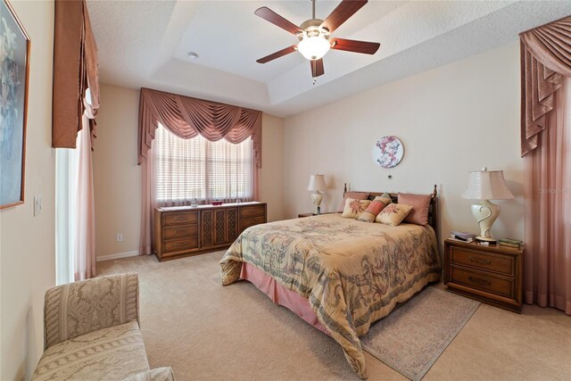 bedroom with ceiling fan, a textured ceiling, a raised ceiling, and light carpet