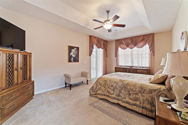 bedroom with a tray ceiling, ceiling fan, light colored carpet, and a textured ceiling